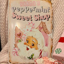 Pink Santa's Peppermint Sweet Shop Metal Sign on bed